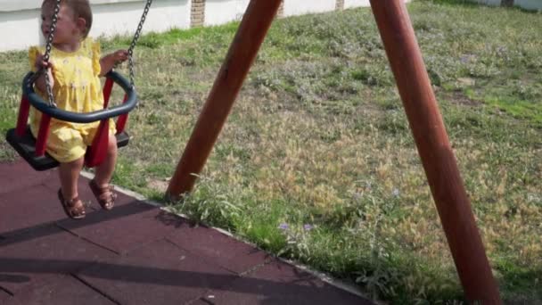 Счастливый ребенок на качелях в летний день на детской площадке. Медленное движение — стоковое видео