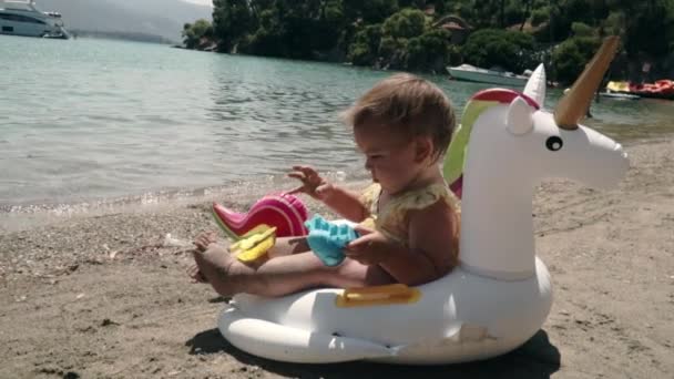 Rainbow unicorn toy and baby on the beach. Summer vacation to the sea. Greece — Stock Video