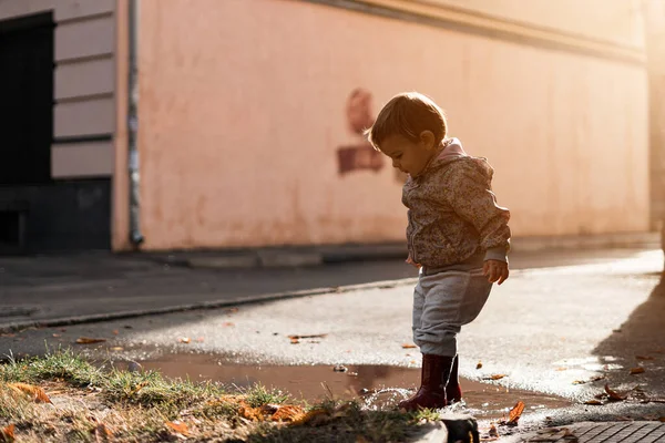 Niña con botas rojas jugando en charco después de la lluvia. Feliz caída actividad de la infancia —  Fotos de Stock