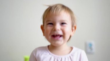 Küçük kız portresi gülümsüyor ve zıplıyor. Evde mutlu çocuk bakıcıları var.