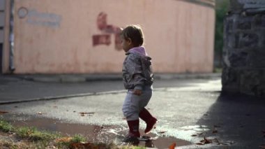 Su birikintisinde oynayan kırmızı çizmeli küçük bir çocuk. Neşeli sonbahar aktivitesi