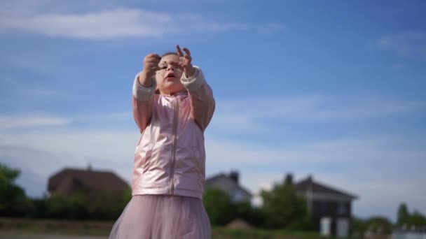 Маленькая девочка в розовом плаще на фоне голубого неба. Счастливый беззаботный ребенок — стоковое видео