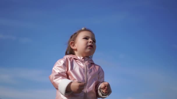 Niña pequeña en impermeable rosa sobre retrato de fondo de cielo azul. Feliz niño libre de preocupaciones — Vídeos de Stock