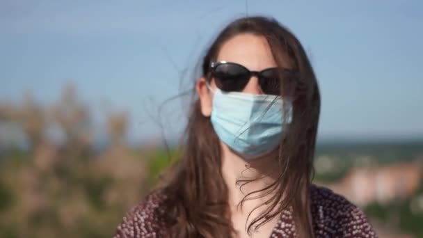 Giovane donna con maschera medica viso e occhiali da sole all'aperto il giorno d'estate. nuova normalità — Video Stock