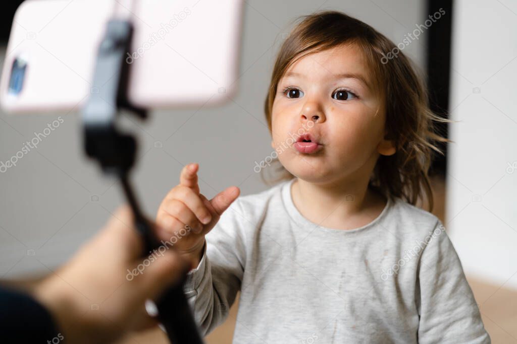 Toddler girl using phone with selfie stick to call grandparents. Virtual connection of people