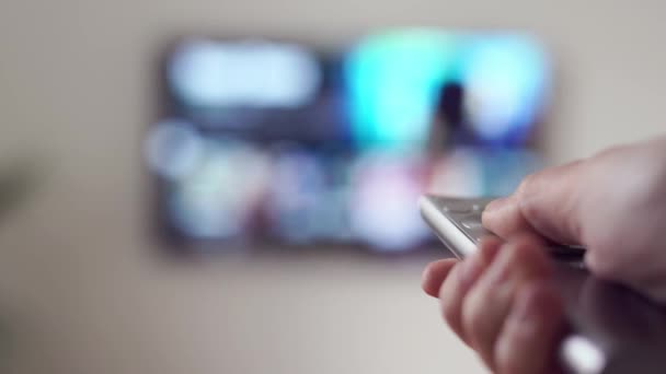 Mulher sentada no sofá na sala de estar com controle remoto de TV e assistindo VOD plataforma de streaming online — Vídeo de Stock