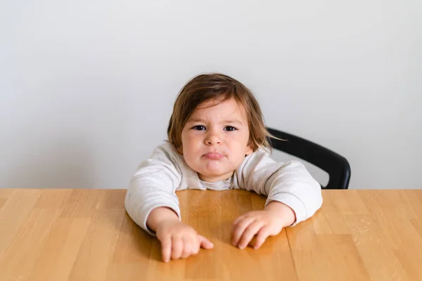 Toddler girl unhappy sitting at wooden desk. Tired child, hungry kid — Stockfoto
