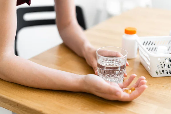 Womans hands with supplements pills and glass of water. Self health care with preventive medicine