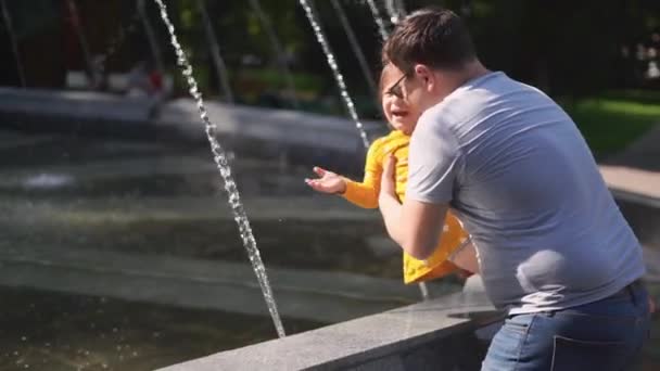 Маленькая девочка с отцом, играющая с фонтаном в замедленной съемке. летняя активность с детьми на открытом воздухе — стоковое видео