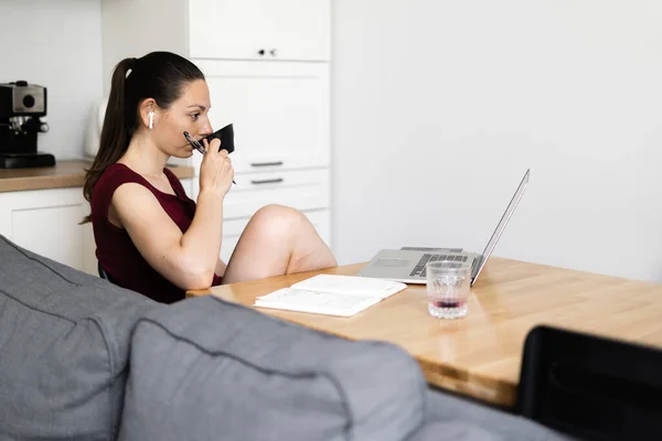 A mulher milenar trabalha em casa. Cozinha com mesa de madeira e xícara de café. E-learning — Fotografia de Stock