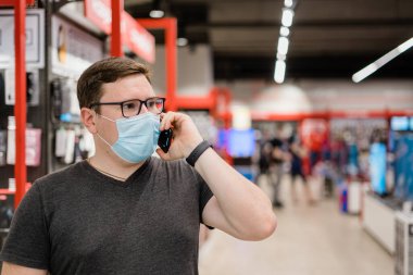 Beyaz adam tıbbi maskeli giysiler için alışveriş yapıyor. Yeni normal kavram. 