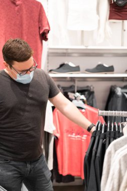 Beyaz adam tıbbi maskeli giysiler için alışveriş yapıyor. Yeni normal kavram. 