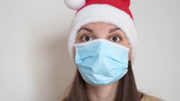 Mujer caucásica se pone máscara médica y sombrero de navidad santa. Celebración de Navidad en encierro — Vídeo de stock
