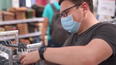 Beyaz adam tıbbi maskeli giysiler için alışveriş yapıyor. Yeni normal kavram. 