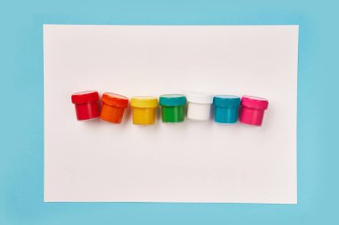 Beyaz tuval üzerinde gökkuşağı renkli boya şişelerinin üst görüntüsü