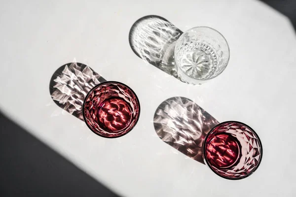 Crystal red glass on white table. Hard shadows in sunlight. — Stock Photo, Image