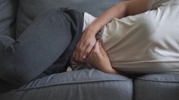 Γυναίκα με πόνο στην κοιλιά ξαπλωμένη στον γκρι καναπέ. Επώδυνες περίοδοι. Προβλήματα πεπτικού συστήματος. — Αρχείο Βίντεο