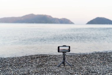 Monopod çubuğundaki akıllı telefon. Deniz günbatımının video kaydı. İçerik oluşturucu