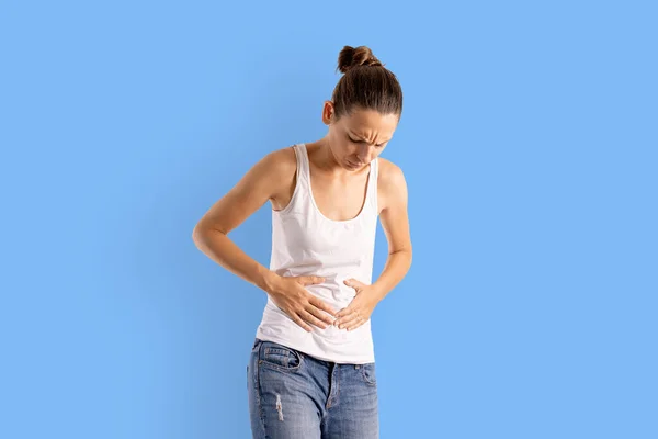 Caucasian woman with abdomen pain. Painful menstruation, digestive problem. Blue background