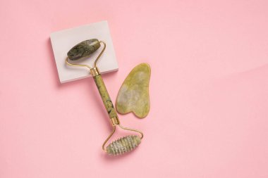Pembe arka planda Guasha yeşil doğal değerli taş yuvarlak. Yaşlanma karşıtı kişisel bakım aracı. 