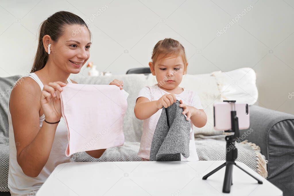 Mother with child streaming online video of unboxing clothes. Influencer occupation, mommy blog