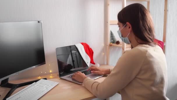 Ung kvinna i tomte hatt och julbelysning på kontoret ensam. Handla på nätet. Karantänfirande — Stockvideo