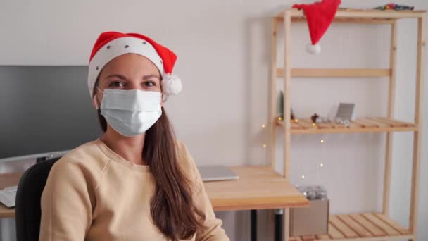 Young woman in santa hat and christmas lights in office alone. Online shopping. Quarantine celebration — Stock Video