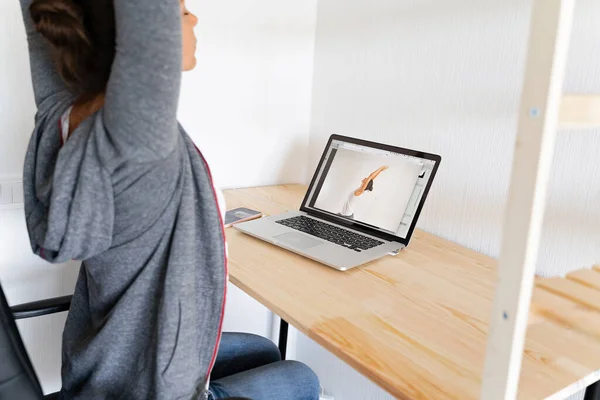 Kvinna gör stretching yoga på sitt kontor genom online sport video. Arbetets ändamålsenlighet. — Stockfoto
