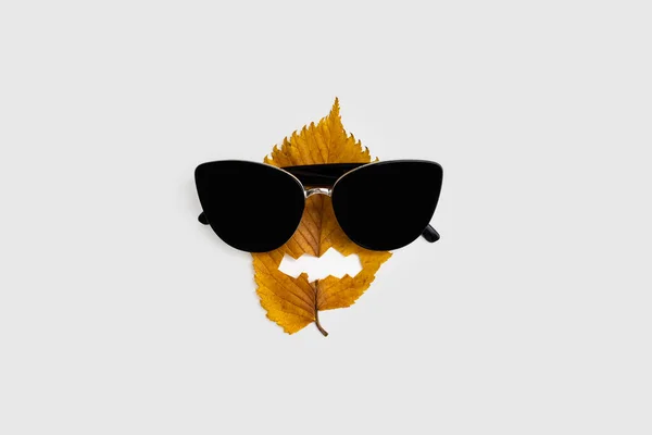 Hoja de otoño amarillo con cara de halloween y gafas de sol. Vacaciones naturales. Mínimo. —  Fotos de Stock