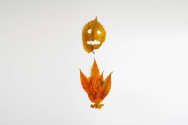 Cadılar bayramı yüzlü sarı sonbahar yaprağı ve beyaz arka planda izole edilmiş ateş. Ürkütücü minimal tatil