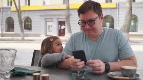 Kaukázusi apa kisgyerekkel a kávézóban. Online telefonos munka gyerekekkel. — Stock videók