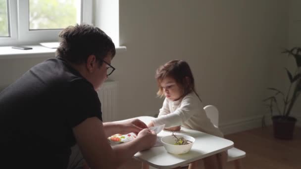 Кавказский отец с ребенком дома читает книгу и ест виноград. Домашнее обучение во время карантина. — стоковое видео