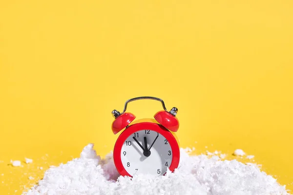 Reloj despertador rojo retro con nieve sobre fondo amarillo. Navidad creativa o concepto de año nuevo. — Foto de Stock