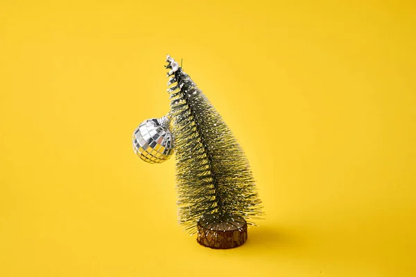 Palla da discoteca e albero di Natale piegato su sfondo giallo grassetto. Divertente festa post sbornia, stile festa anni '90 — Foto Stock