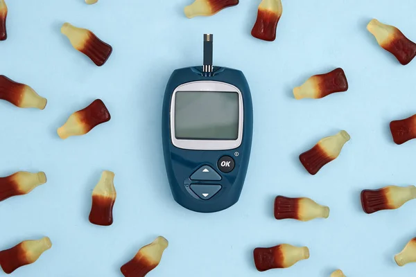 Top view of glucose meter and sweet jelly candies on blue background. Diabetes, high blood sugar level problem