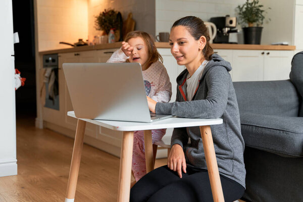 Mother and child girl sitting at home ad watching school video on laptop. Distant education, homeschooling kids.