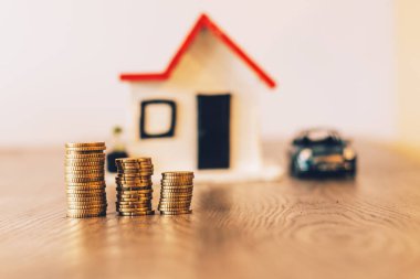 Paralar yığılmış bir bulanık ev ve araba arka planda ile ahşap bir masa üstünde: Emlak, gayrimenkul yatırım, evi ipotek, tasarruf mali kavramı.