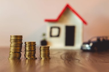 Paralar yığılmış bir bulanık ev ve araba arka planda ile ahşap bir masa üstünde: Emlak, gayrimenkul yatırım, evi ipotek, tasarruf mali kavramı.