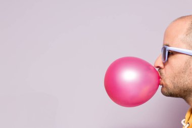 Resmin sağ tarafında yer pembe sakız şişirme mor gözlüklü adam