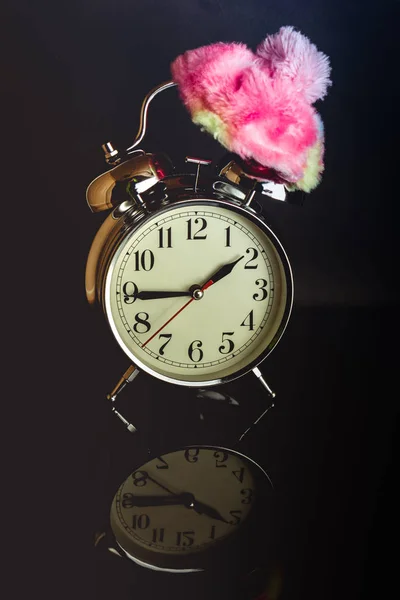 White retro clock with a winter hat isolated against a dark background casting a reflection