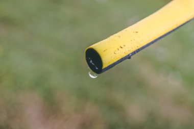 Bir hortum boru su damlıyor ve çim zemin üzerine bir damla ile yakın çekim