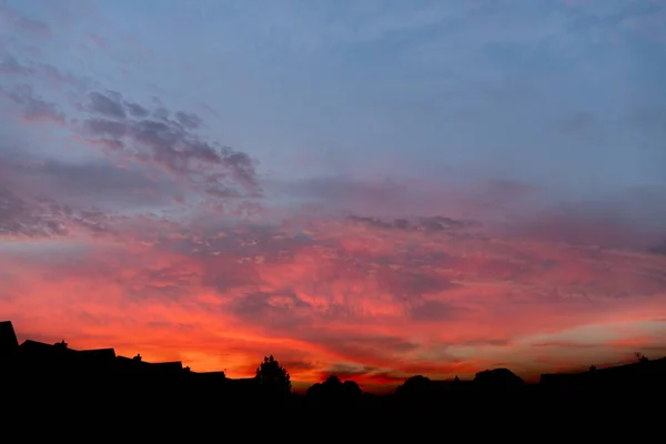 Details of clouds at sunset with dark orange, pink, and blueish purple tones above the silhouette of houses in the darkness