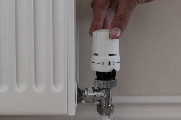 Hand turning the radiator knob to lower the heat and save on consumption and energy