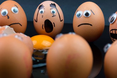 Eğlenceli kavramı: çiğ yumurta ile googly eyes ve çizilmiş şekil vardır şok ve onlar gördüğünüz gibi üzgün başka bir yumurta beyaz ve sarısı önlerinde; iki kırık koyu arka plan.