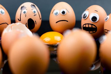 Eğlenceli kavramı: çiğ yumurta ile googly eyes ve çizilmiş şekil vardır şok ve onlar gördüğünüz gibi üzgün başka bir yumurta beyaz ve sarısı önlerinde; iki kırık koyu arka plan.