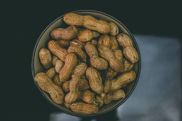 Roasted peanuts inside a black bowl against dark background