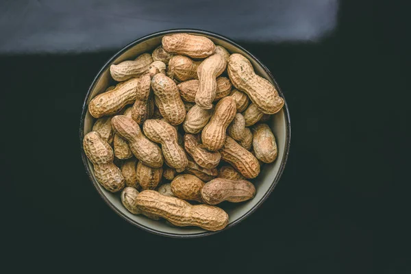 Roasted peanuts inside a black bowl against dark background