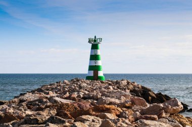 Kayalık bir iskelenin sonunda yeşil ve beyaz bir deniz feneri