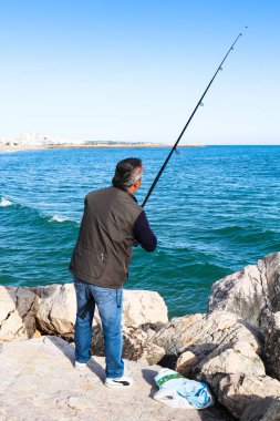 16 Nisan 2019, Vilamoura, Portekiz - plaja yakın kayalık bir iskelenin kenarında balık avlamak