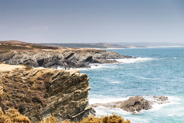 An unidentified man stands near a cliff facing the sea in the village of Porto Covo, Portugal